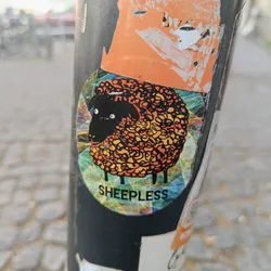 A round sticker featuring a stylized black sheep with orange and yellow wool against a colorful, geometric background. The word SHEEPLESS is printed below the sheep.