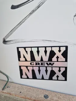 A holographic NWX Crew sticker with a black background and white/holographic lettering. The sticker is rectangular and has the text 'NWX' on top and bottom, with 'CREW' in the middle.