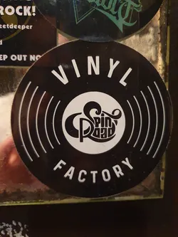 Black and white sticker with the text VINYL FACTORY and a logo in the center. The logo is a stylized record with the text Spin Road inside.