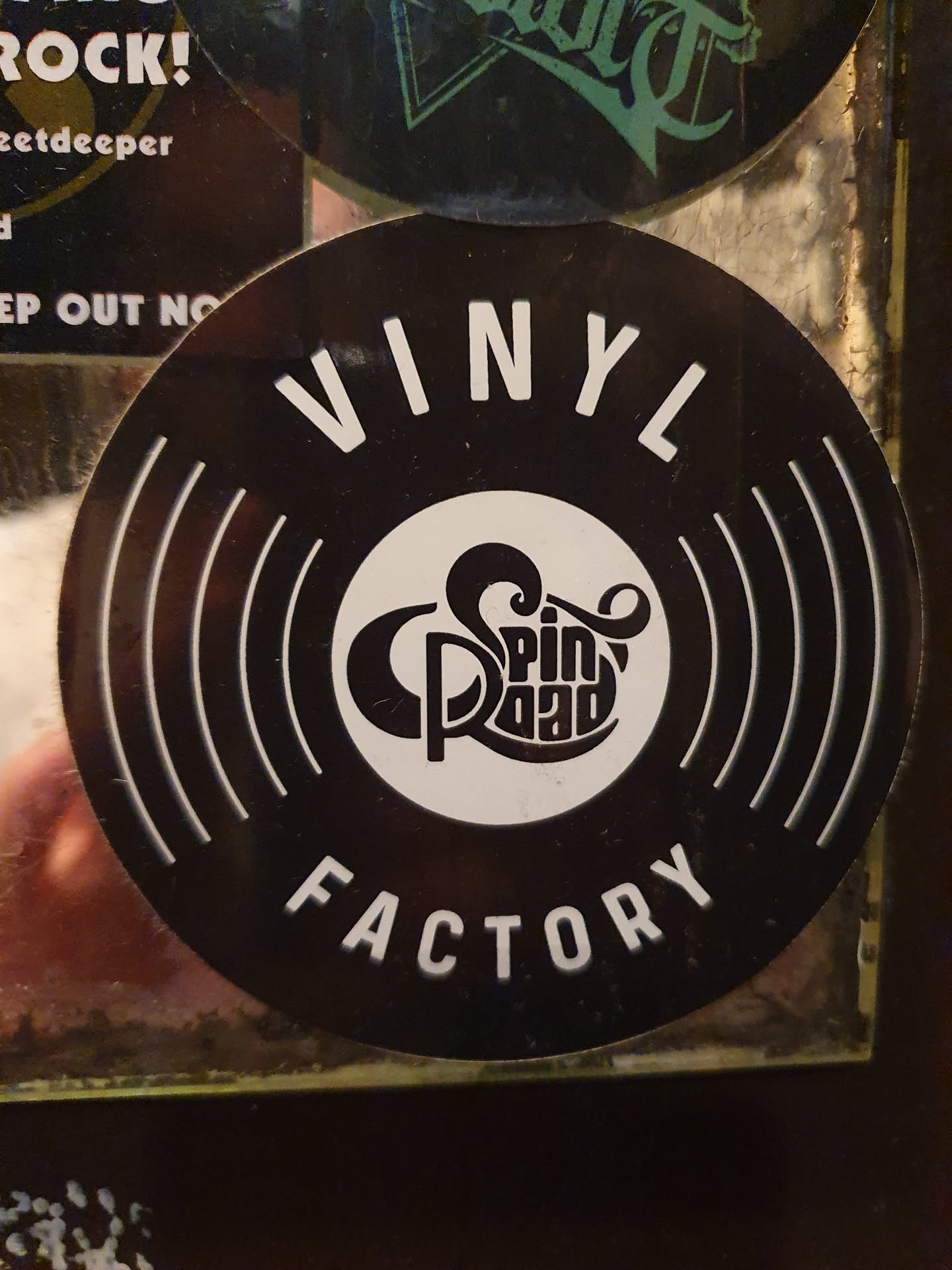 Black and white sticker with the text VINYL FACTORY and a logo in the center. The logo is a stylized record with the text Spin Road inside.