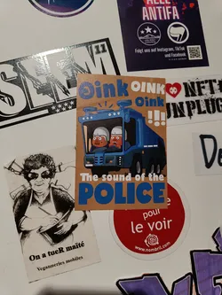 A sticker with a cartoon illustration of a police truck with two pig-like characters inside. The text on the sticker says "Oink Oink Oink" and "The sound of the police".