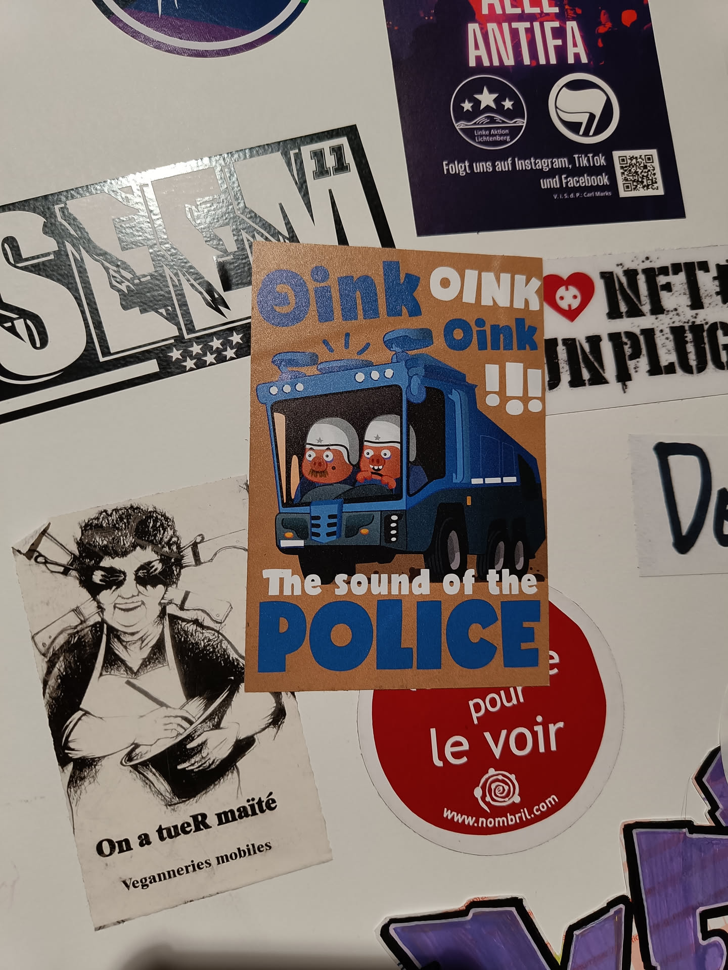 A sticker with a cartoon illustration of a police truck with two pig-like characters inside. The text on the sticker says "Oink Oink Oink" and "The sound of the police".