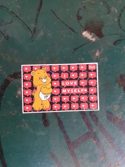 A sticker featuring a Care Bear hugging itself, surrounded by social media like icons. The text on the sticker reads "I LOVE MYSELF". The sticker is on a dark teal surface.