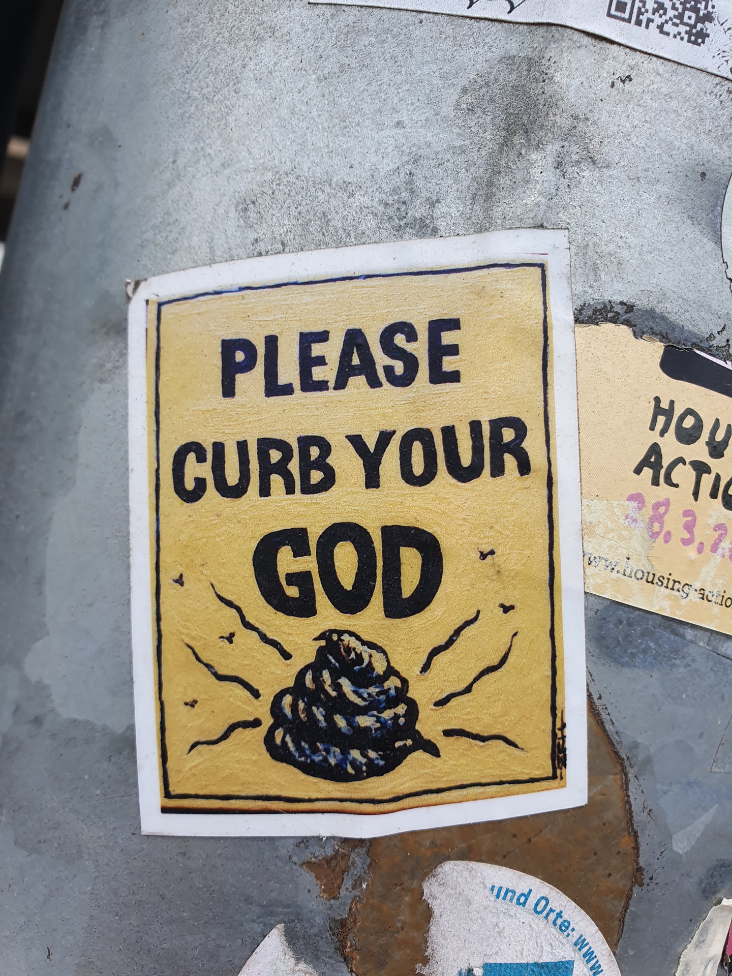 A yellow sticker with a drawing of a pile of poop and the text "Please curb your god".