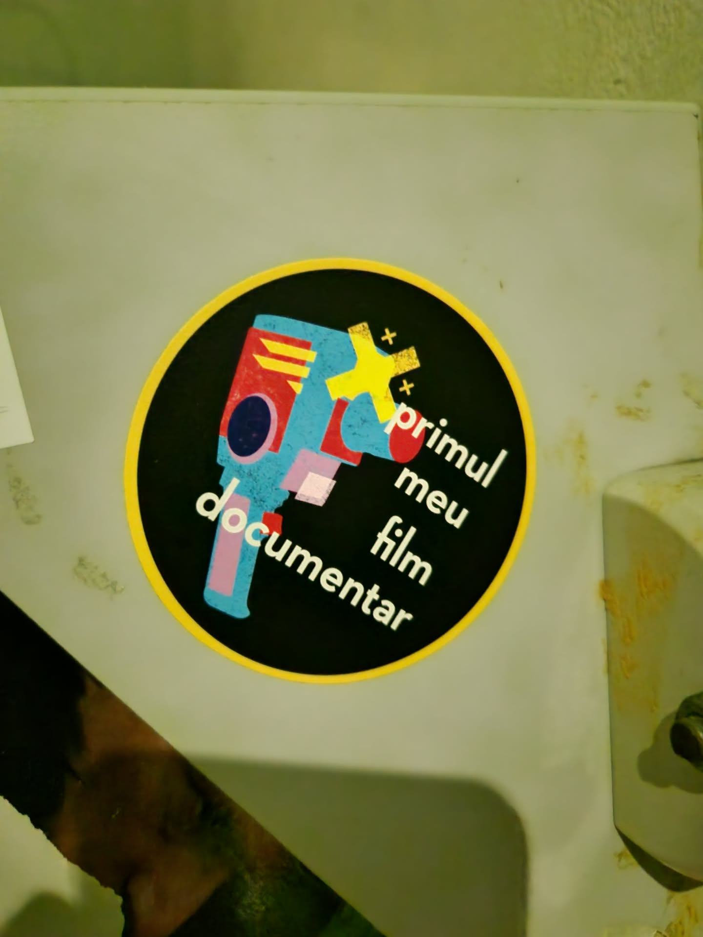 Round sticker with a illustrated camera and text in portuguese. The text says: "meu primeiro filme documentar" which means in english: "my first documentary film"
