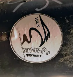 Round sticker with a drawing of a bird and the word VOLK above it. Below the bird are small boxes with German political party names: LINKE, AFD, CSU, BSU, FDP, SPD, CDU, and GRÜNE. At the bottom, the word FREIHEIT (freedom) is written. The sticker seems to be a political statement.