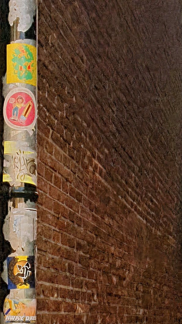 The image features a pole covered with various stickers set against a backdrop of a brick wall. The stickers are colorful and feature different designs. One sticker depicts a figure with a pencil and appears to warn against something, due to the red circle and bar over the image.