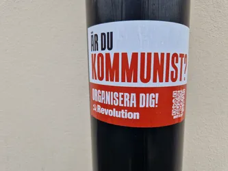 A red and white sticker with the text "Är du kommunist?" (Are you a communist?) and "Organisera dig!" (Organize yourself!). It also features a QR code and the word "Revolution" with a hammer and sickle symbol.