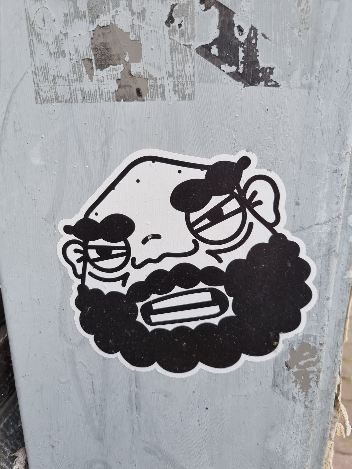 Black and white sticker of a man with a beard. He has a grumpy expression and seems to be scowling. The style is simple and cartoonish.