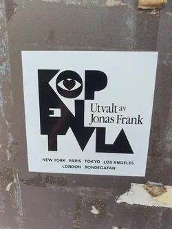 Black and white sticker with the text "KOPENTVL" stylized with geometric shapes and an eye symbol with a heart in the middle. It also features the text "Utvalt av Jonas Frank" and a list of cities: New York, Paris, Tokyo, Los Angeles, London, and Bondgatan.