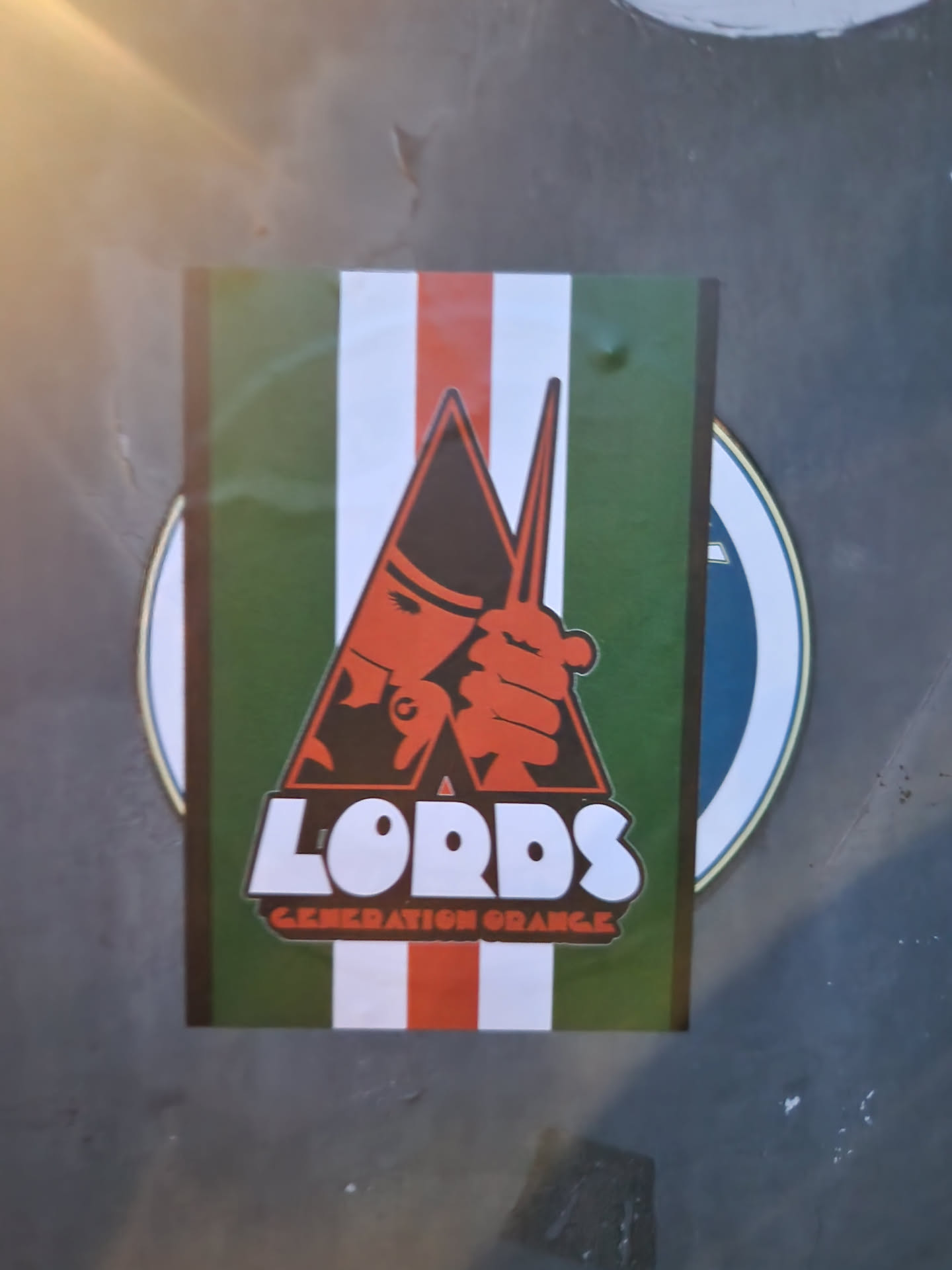 A sticker featuring a stylized illustration of a person holding drumsticks, set against a green and white striped background. The text "LORDS GENERATION ORANGE" is prominently displayed below the illustration.