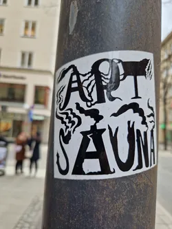 Black and white sticker with the words "Art Sauna" in a stylized font. The letters are surrounded by abstract designs resembling smoke or steam.