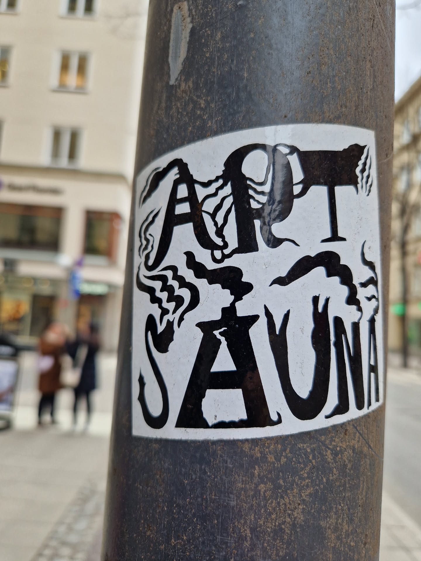 Black and white sticker with the words "Art Sauna" in a stylized font. The letters are surrounded by abstract designs resembling smoke or steam.