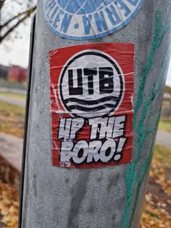 A red and white sticker with the acronym UTB and the words "Up The Boro!" in a comic sans font. The sticker is attached to a metal pole.