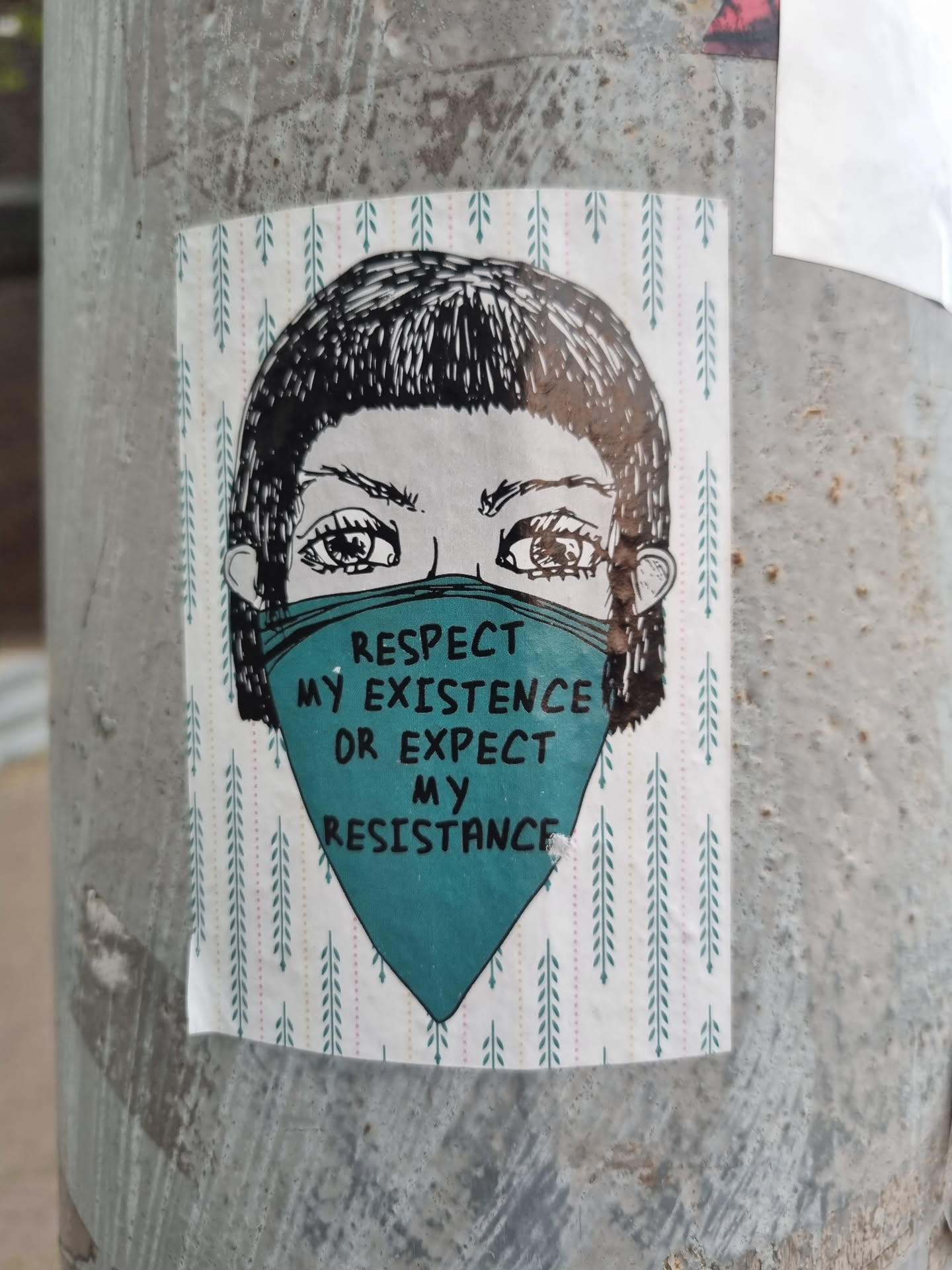 A sticker featuring a stylized illustration of a person's face wearing a teal mask. The mask has the text  "Respect my existence or expect my resistance" on it. The background of the sticker is a pattern of small, stylized pine tree branches. 