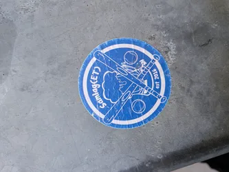 The sticker is circular with a blue background and a white border. In the center, two crossed baseball bats are depicted, with a baseball above them. A stylized cloud-like shape is visible behind the bats. Text is present along the circumference: 'Samlag(ET)' on the left and 'est 2016' on the right. The overall design is simple and graphic, suggesting a sports team or organization.