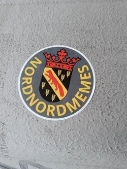 Round sticker with a coat of arms featuring a fox and wheat, surrounded by the word NORDMEMES. 