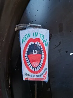 A sticker with an illustration of a mouth saying "New in Town". The sticker is designed by Javier Garcia Tattoo.