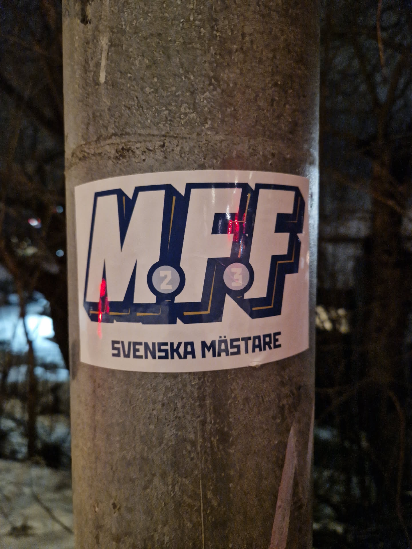 A sticker featuring the MFF logo and the text "Svenska Mästare" (Swedish Champions). The logo appears to be a stylized representation of the letters MFF with numbers 2 and 3 incorporated into the design. 
