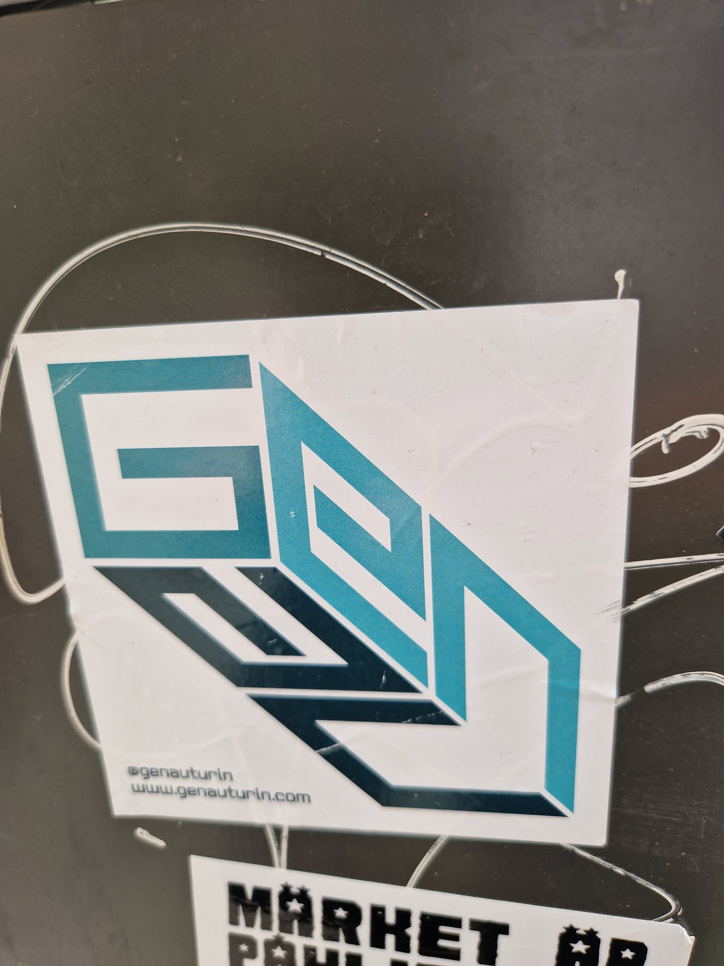 A teal and black logo sticker with the text "GENA" stylized in a 3D, geometric design.  The sticker also includes the text "@genauturin" and "www.genauturin.com".