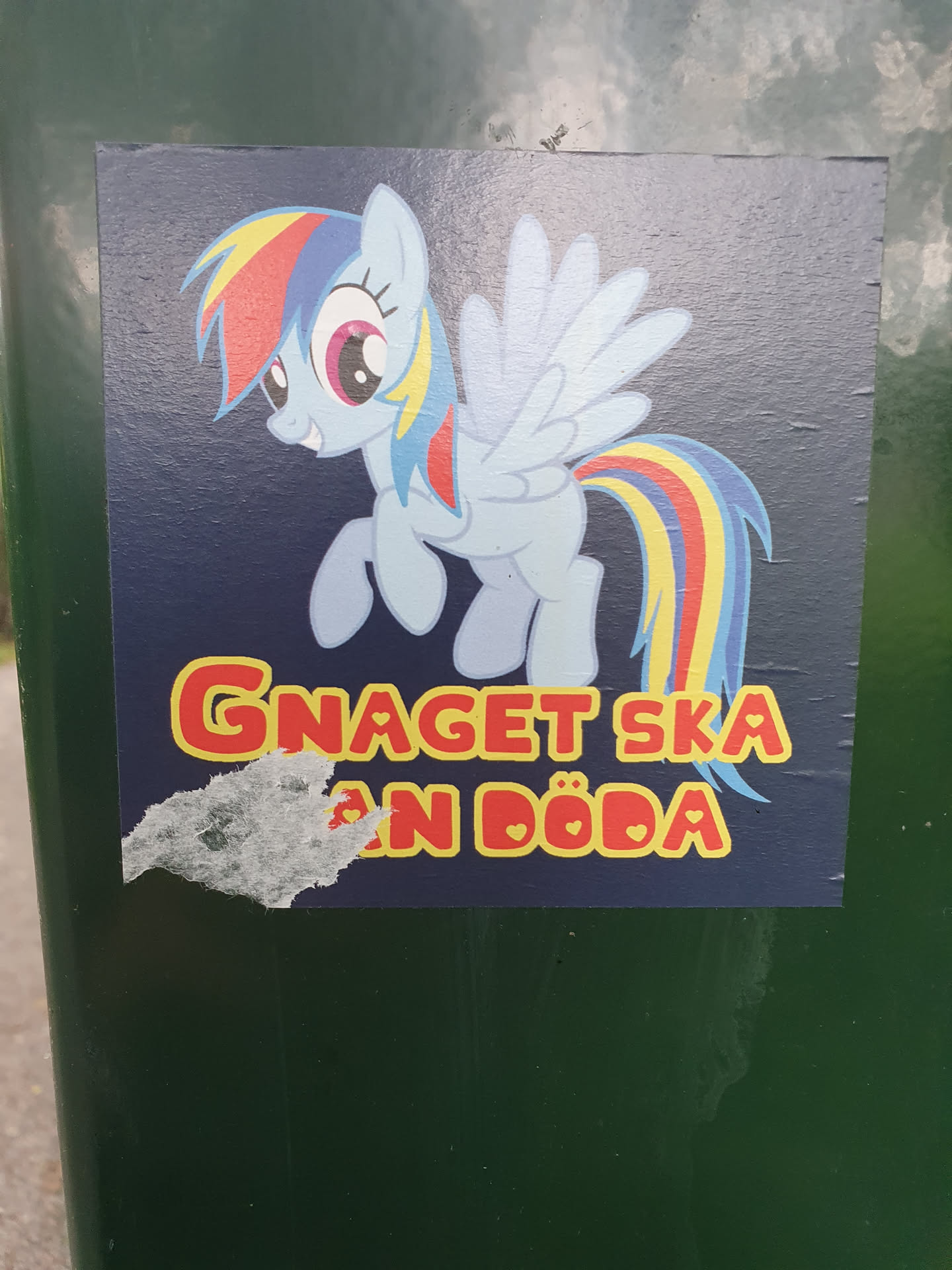 A sticker featuring Rainbow Dash from My Little Pony, with Swedish text that translates to something like: "The gnawing must die" or "The nibbling must die".  The sticker is slightly damaged.
