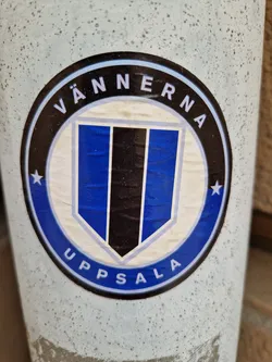 A round sticker with a blue and black crest.  The text "VÄNNERNA" is written in a circle around the crest, with "UPPSALA" at the bottom.