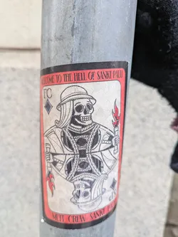 A sticker featuring a skull character in the style of a playing card, with flames and text. It seems to be from a group called "Met Crew Sankt Pauli".