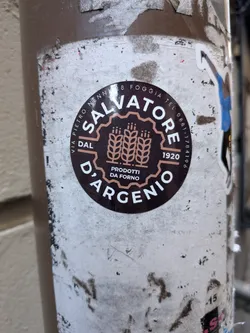 A round, dark brown sticker featuring a bakery logo. The name 'SALVATORE' is arched across the top in white, sans-serif capital letters, while 'D'ARGENIO' curves along the bottom. In the center, framed by a scalloped border, are three stylized tan wheat stalks with the words 'PRODOTTI DA FORNO' underneath. To the left and right of the central emblem are the words 'DAL' and '1920' respectively. Small white text along the upper outer rim reads 'VIA PIETRO NENNI 28 FOGGIA TEL 0881-1784196'.