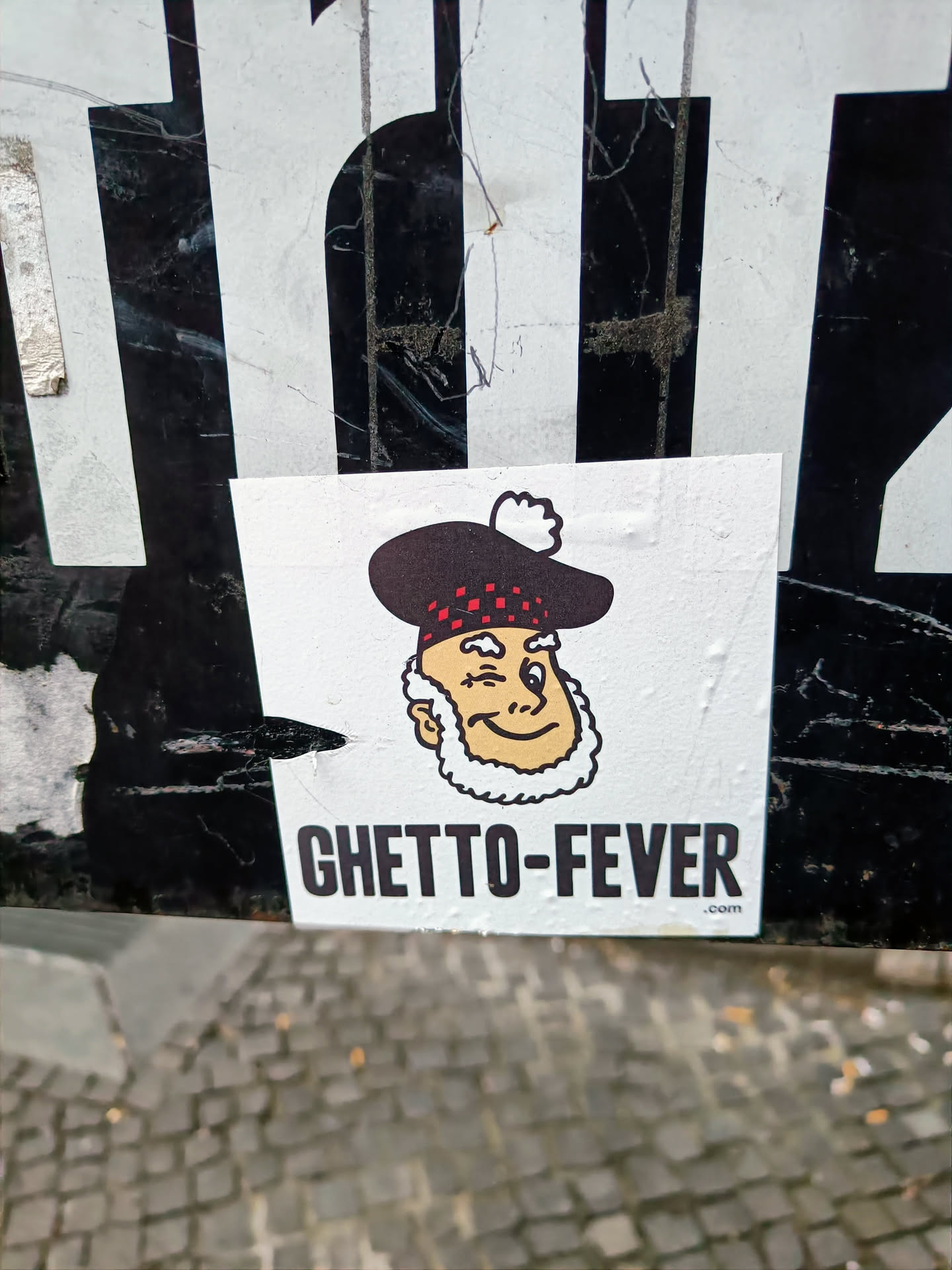 A sticker featuring a cartoon man in a tam o' shanter, winking, with the text "GHETTO-FEVER.com" below. 