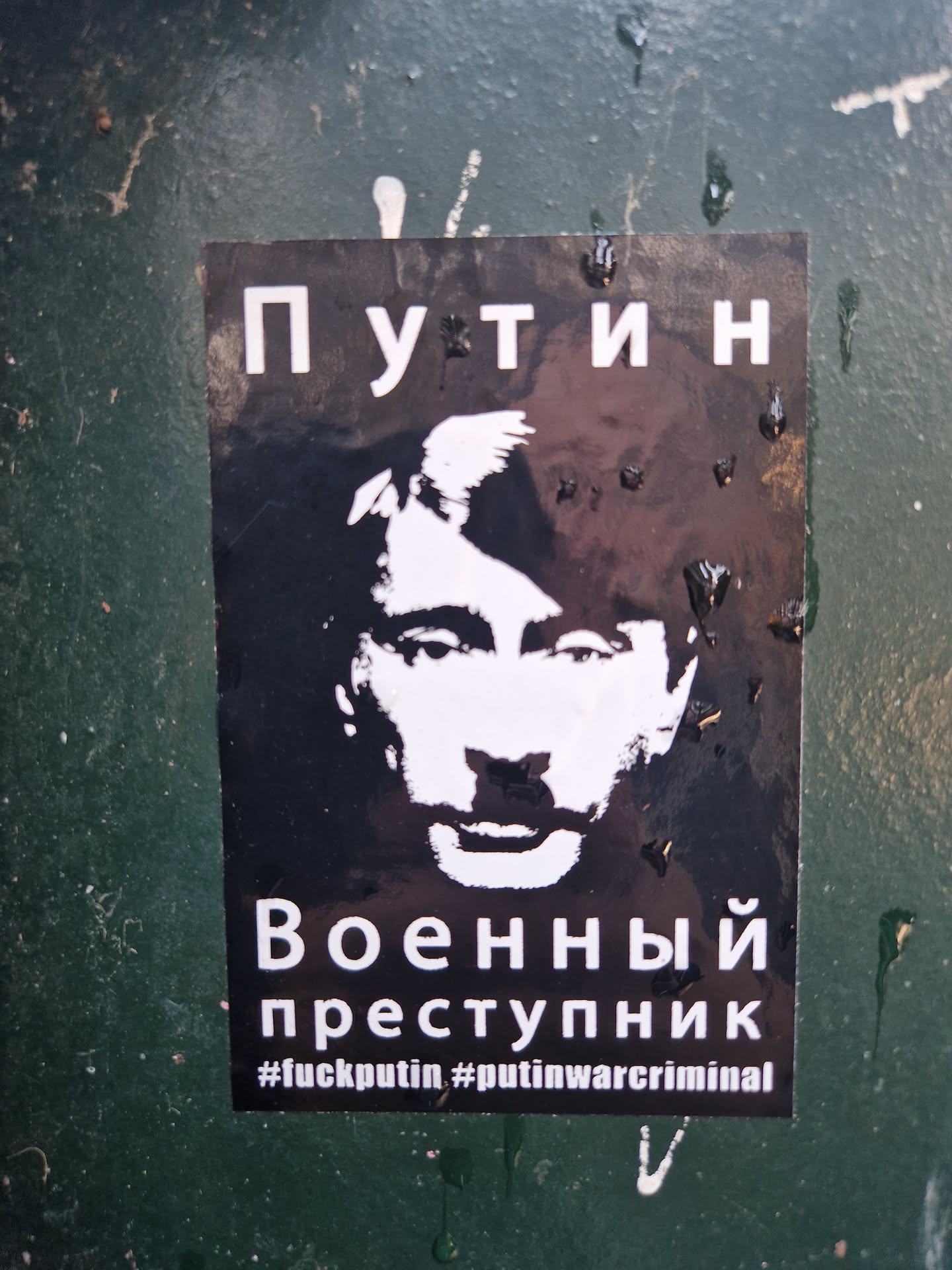 Black and white sticker depicting Vladimir Putin's face with text in Russian and English.  The Russian text translates to "Putin - War Criminal". The English hashtags further emphasize this.