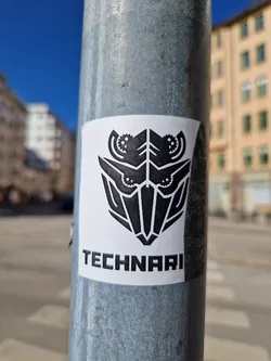 A black and white sticker featuring a stylized robotic or mechanical face with gears.  The word 'TECHNARI' is printed below the graphic.