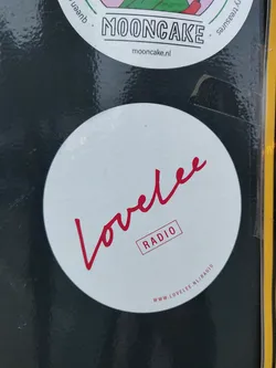 A round white sticker with the word Lovelee written in a red cursive script. Below it, the word RADIO is written in a red box. At the bottom, the website address www.lovelee.nl/radio is printed.