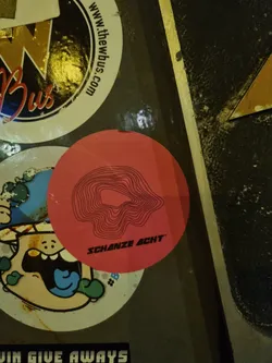 A pink round sticker with a black topographic design and the text "SCHANZE ACHT" printed on it.