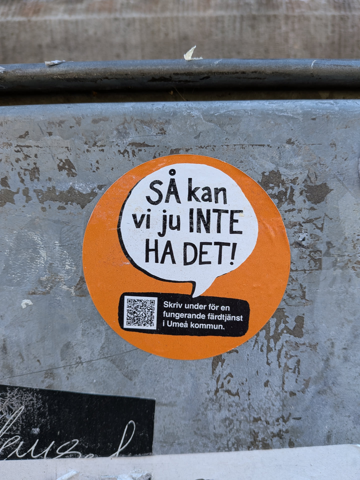The sticker is circular with an orange border and a white speech bubble in the center. The speech bubble contains bold black text that reads 'SÅ kan vi ju INTE HA DET!'. Below the speech bubble, on a black rectangular background, is a QR code and text in Swedish. The text reads 'Skriv under för en fungerande färdtjänst i Umeå kommun.' The overall design is simple and direct, conveying a message of dissatisfaction and a call to action.