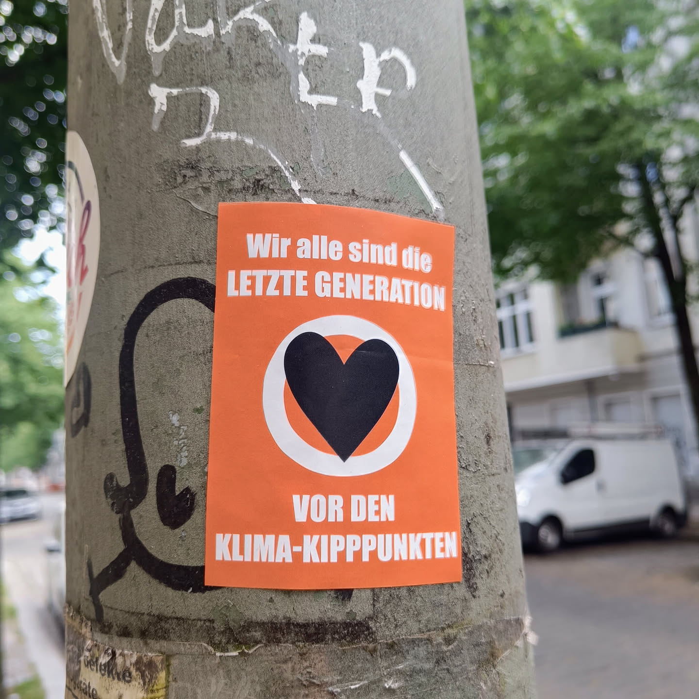 An orange sticker with a black heart in the middle and a text that says: Wir alle sind die letzte Generation vor den Klima-Kipppunkten (We are all the last generation before the climate tipping points)