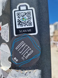 A round sticker for Oyster Bar with a QR code on a separate sticker above it. The QR code contains an image of a van.  Social media links are present at the bottom of the main sticker.
