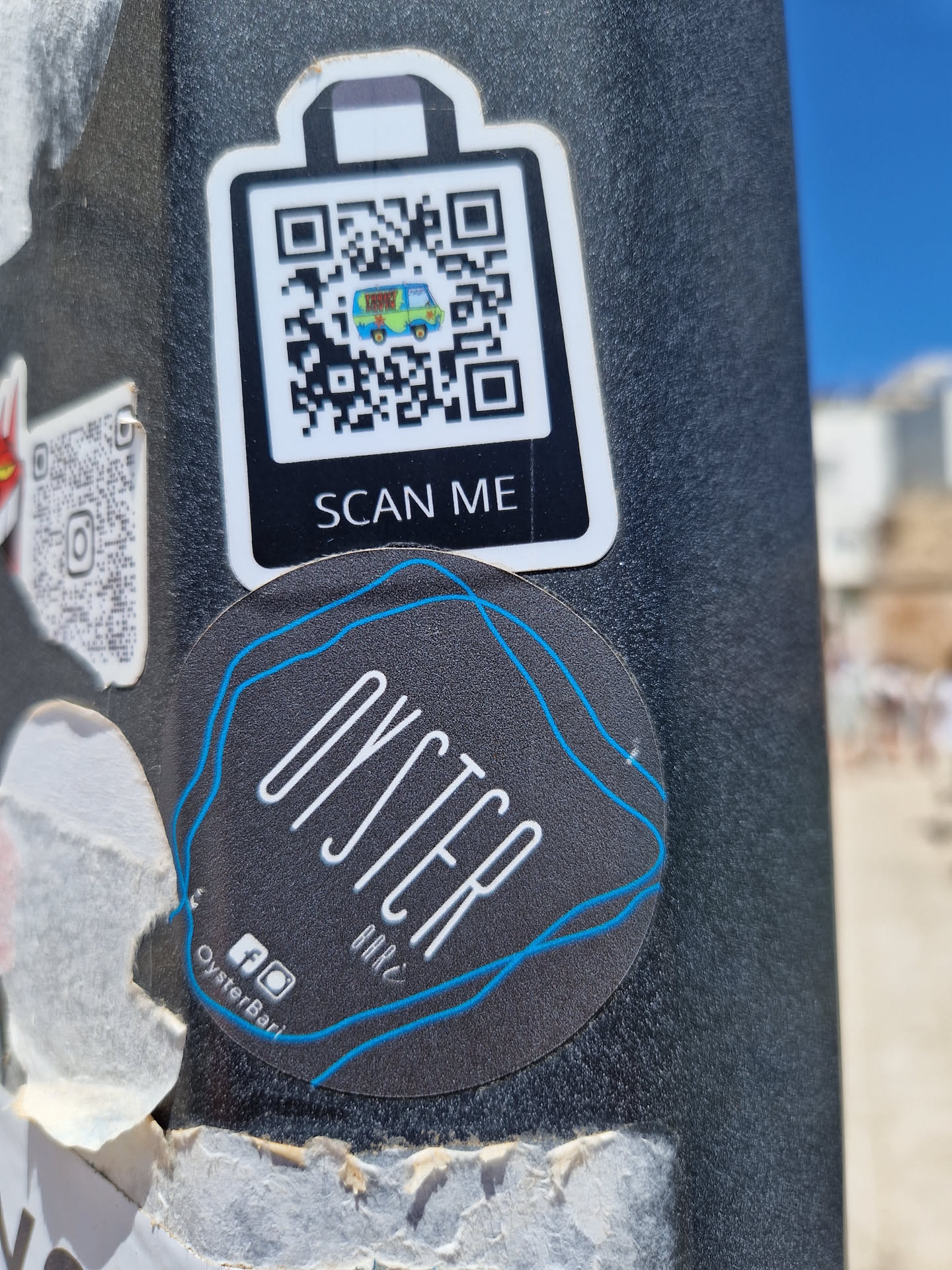 A round sticker for Oyster Bar with a QR code on a separate sticker above it. The QR code contains an image of a van.  Social media links are present at the bottom of the main sticker.