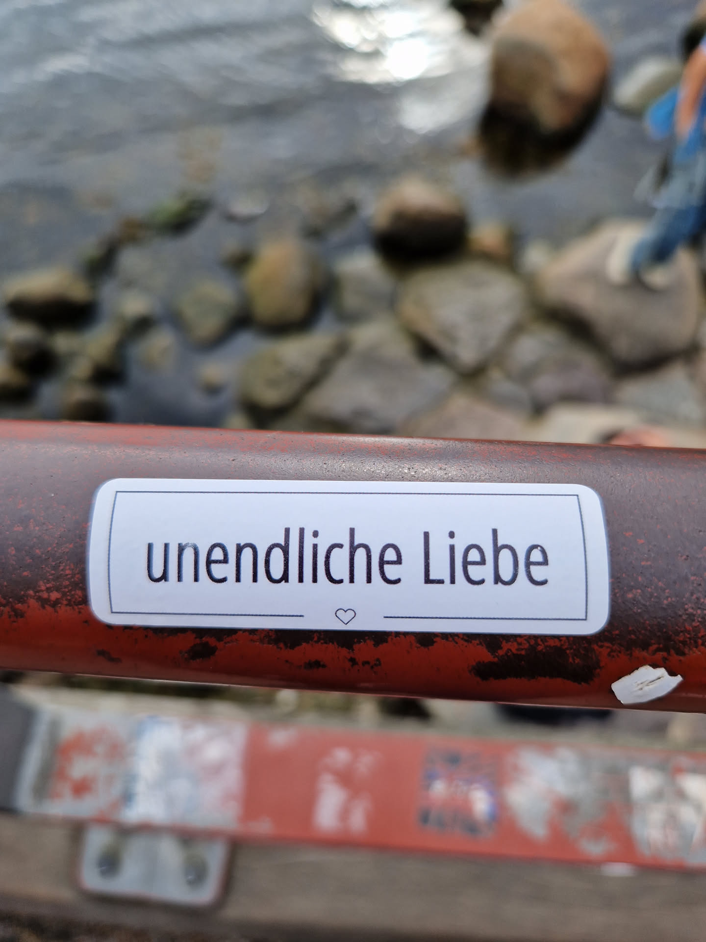 A white sticker on a rusty red metal surface says "unendliche Liebe" (infinite love) in German with a small heart symbol at the end.