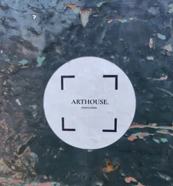 A round white sticker with black text and corner markers on a dark green background. The text reads 'ARTHOUSE. Amsterdam'