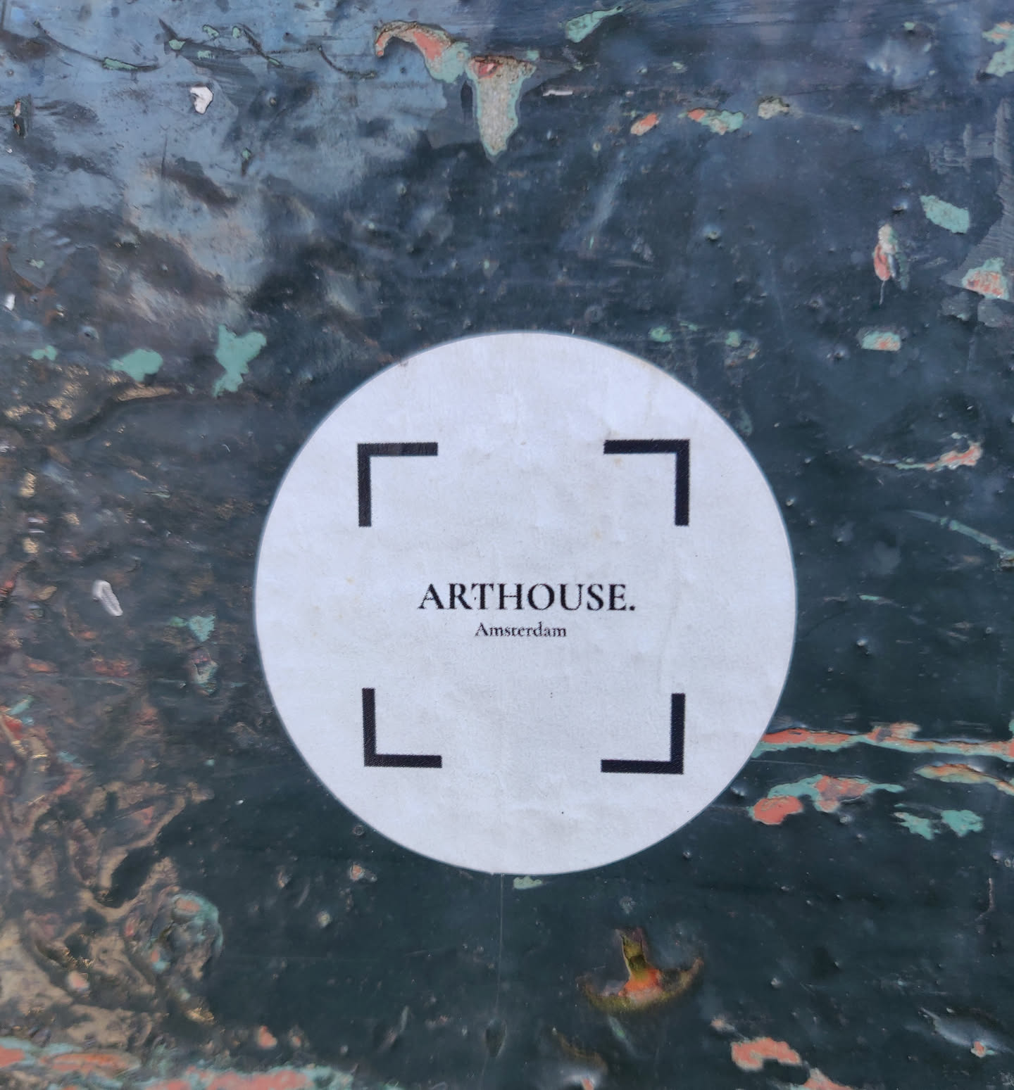 A round white sticker with black text and corner markers on a dark green background. The text reads 'ARTHOUSE. Amsterdam'