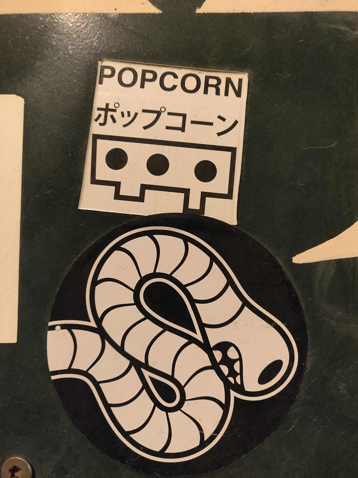 A black and white sticker of a worm design on a black circular background. Above it is a rectangular sticker with the word POPCORN written in English and Japanese.