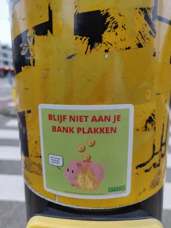 A sticker featuring a burning piggy bank with coins falling on it. The text on the sticker says: "Blijf niet aan je bank plakken" which translates to  "Don't stick to your bank" in Dutch. The sticker also features a small speech bubble with the text "Start nu met duurzaam bankieren". It also contains the logo of DWARS, a Dutch political party.