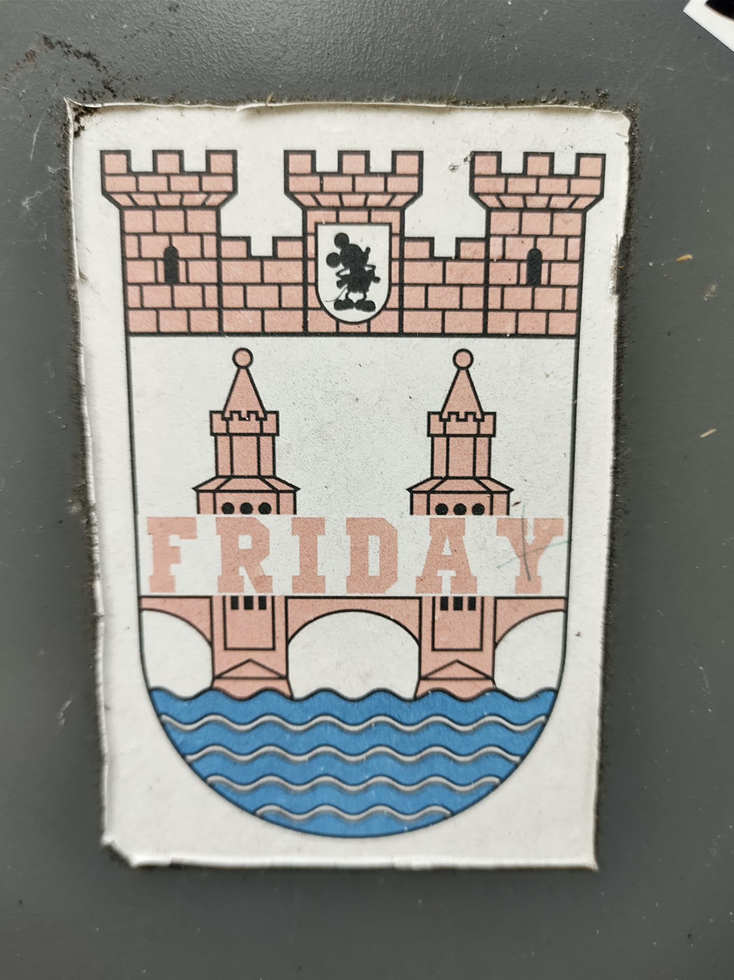 A sticker featuring a coat of arms design with a bridge and the word "FRIDAY" across the middle. The style is simple and playful. 
