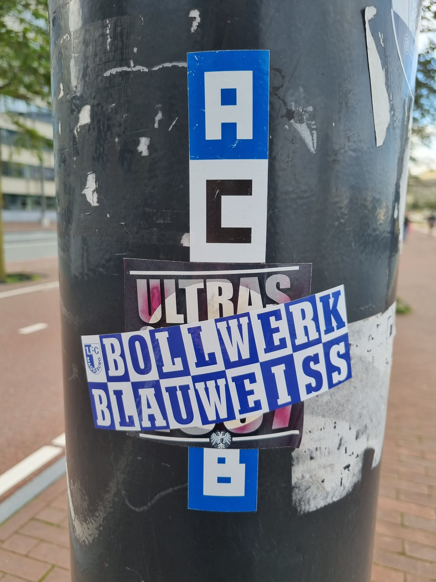 A sticker featuring the text "Bollwerk BlauWeiss Ultras" in a fragmented style.  There are also smaller stickers with the letters "A", "C", and "B" visible nearby.