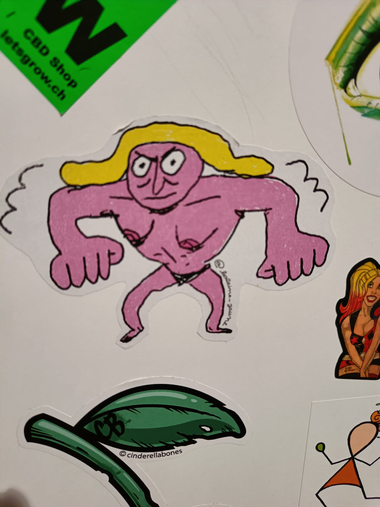 A sticker featuring a cartoon-like illustration of a muscular pink-skinned figure with blonde hair. The character has a somewhat angry expression and is depicted in a slightly aggressive pose. The art style is reminiscent of crude drawings or doodles, with bold outlines and simple shading.  The sticker is likely from an independent artist or brand.