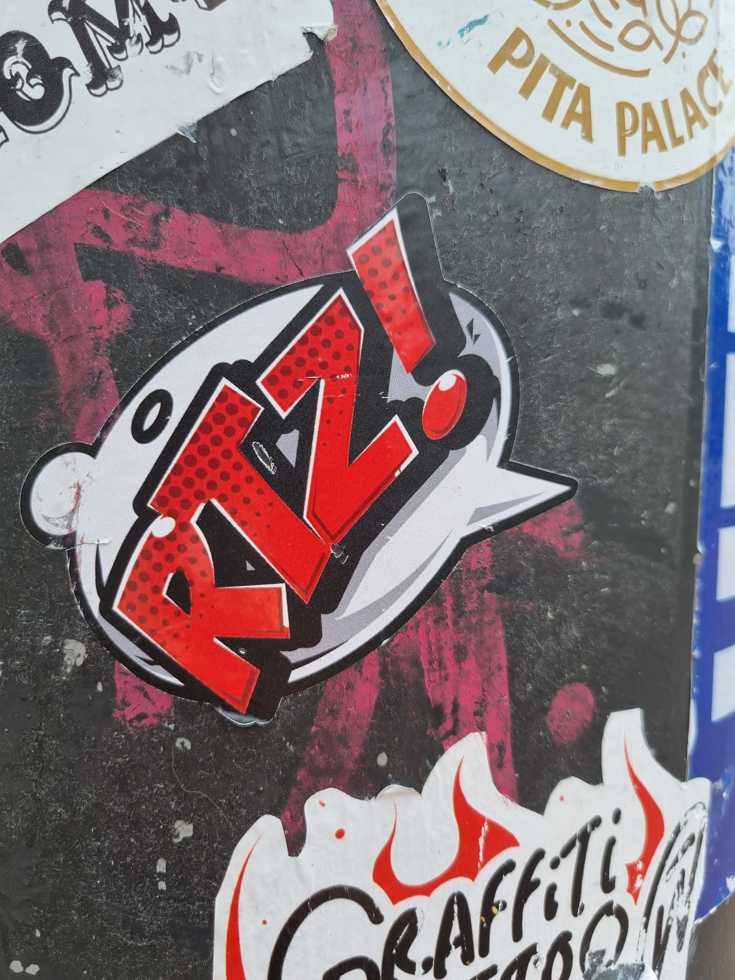 A sticker featuring the stylized text "R!Z!" in a red and white comic book style. The text is contained within a speech bubble with a red exclamation point.  The style is reminiscent of pop art and graffiti.