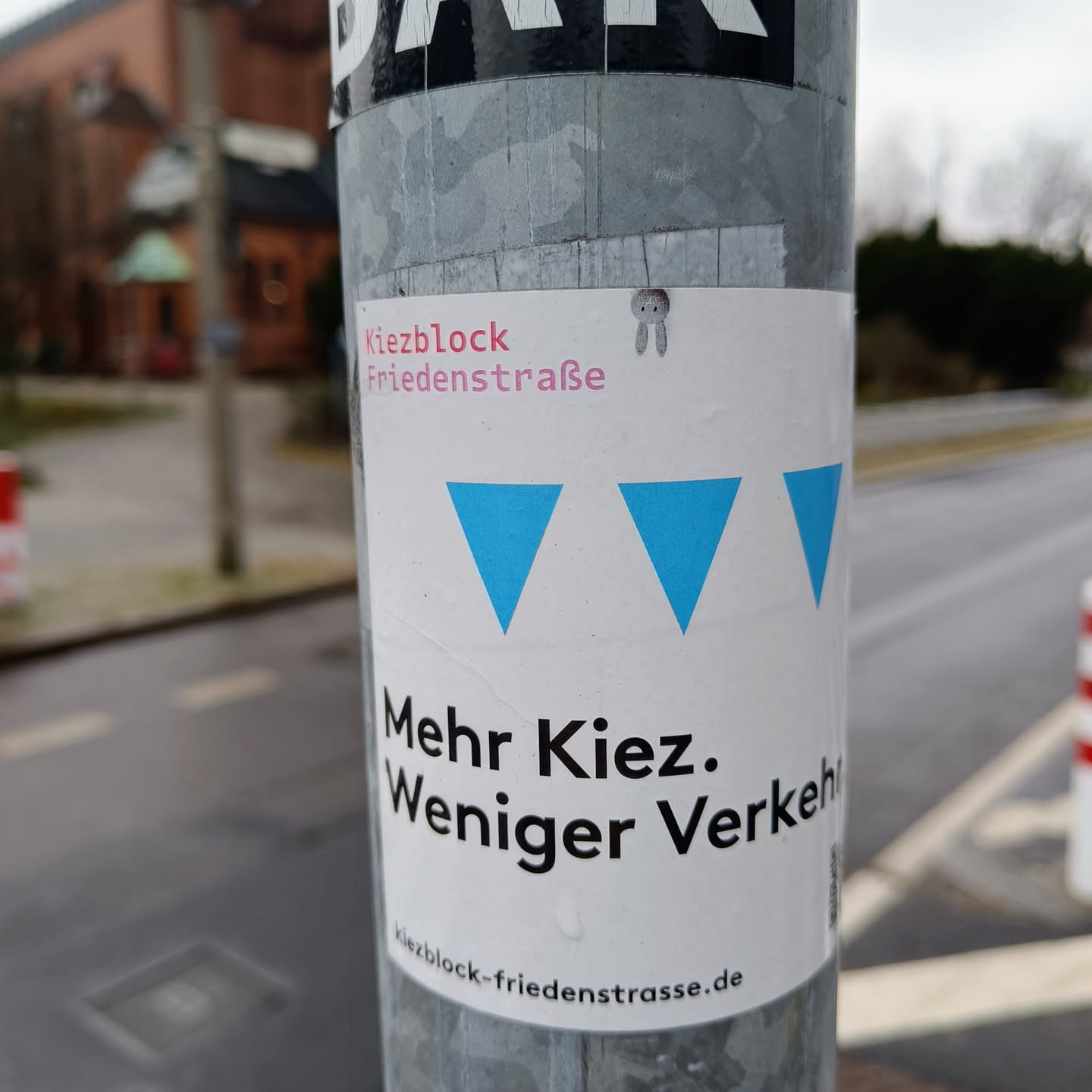 Sticker promoting a neighborhood initiative in Friedensstrasse to prioritize pedestrian and community space over vehicle traffic.  The design features three blue triangles and a website address.