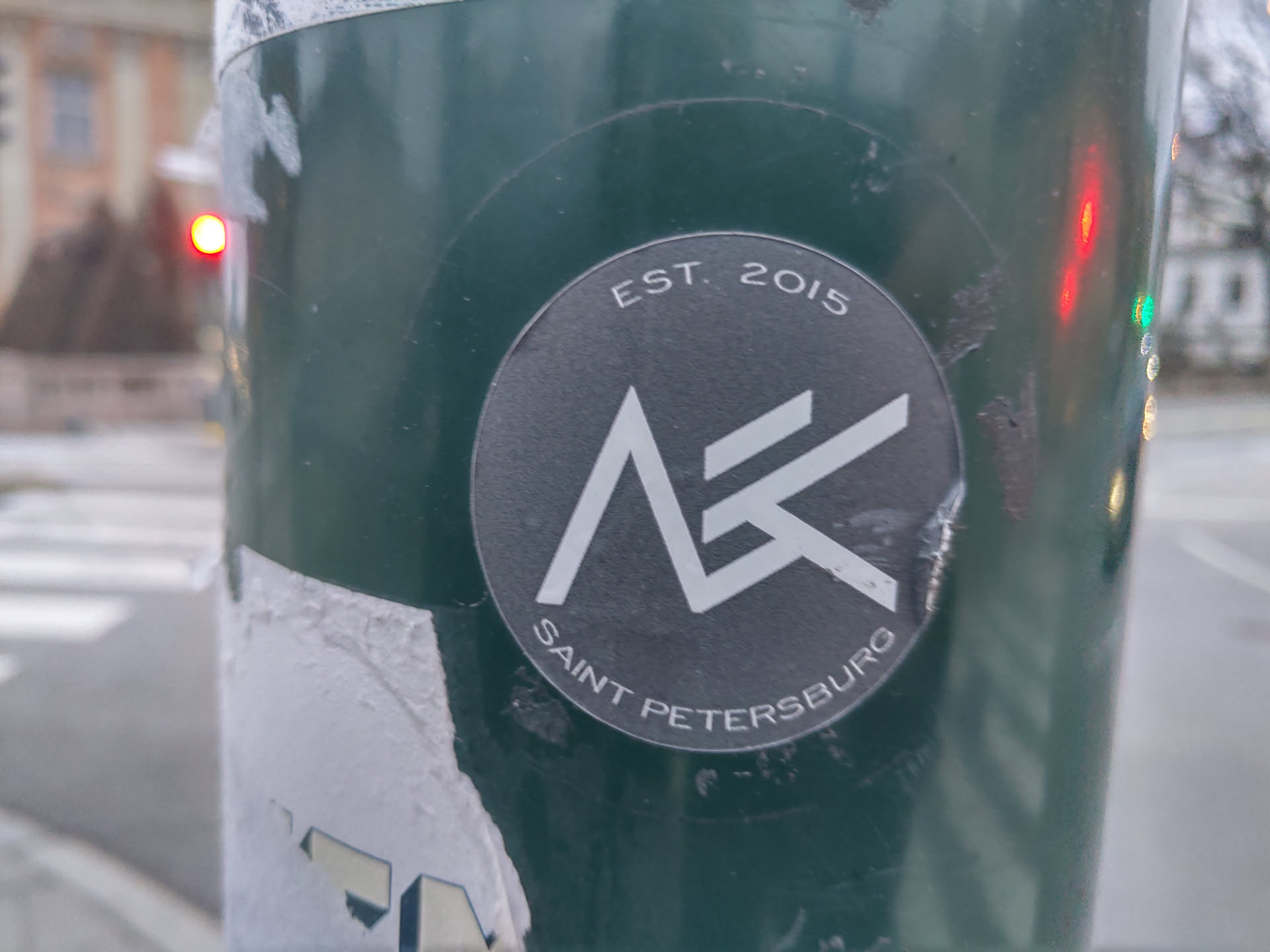 A black and white sticker with a logo and the text 'EST. 2015' and 'SAINT PETERSBURG'. The logo appears to be a stylized letter 'A' or 'K'.