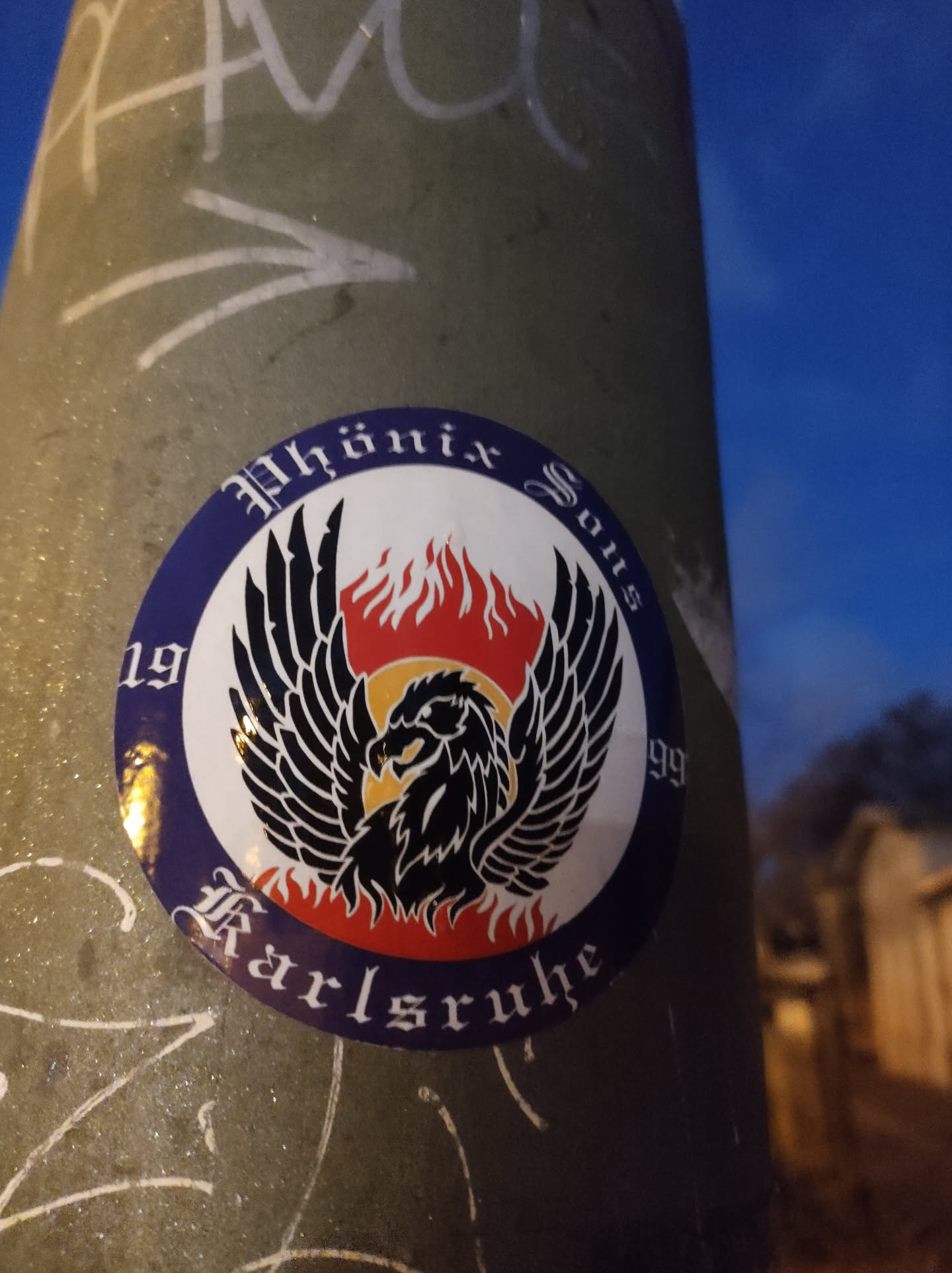 Round sticker featuring a black phoenix with outstretched wings, set against a backdrop of flames. The text 'Phönix Sous' is written in a stylized font above the phoenix, while '1999' is visible on the left and 'Karlsruhe' at the bottom, also in stylized fonts. The colors are primarily blue, red, yellow, and black.