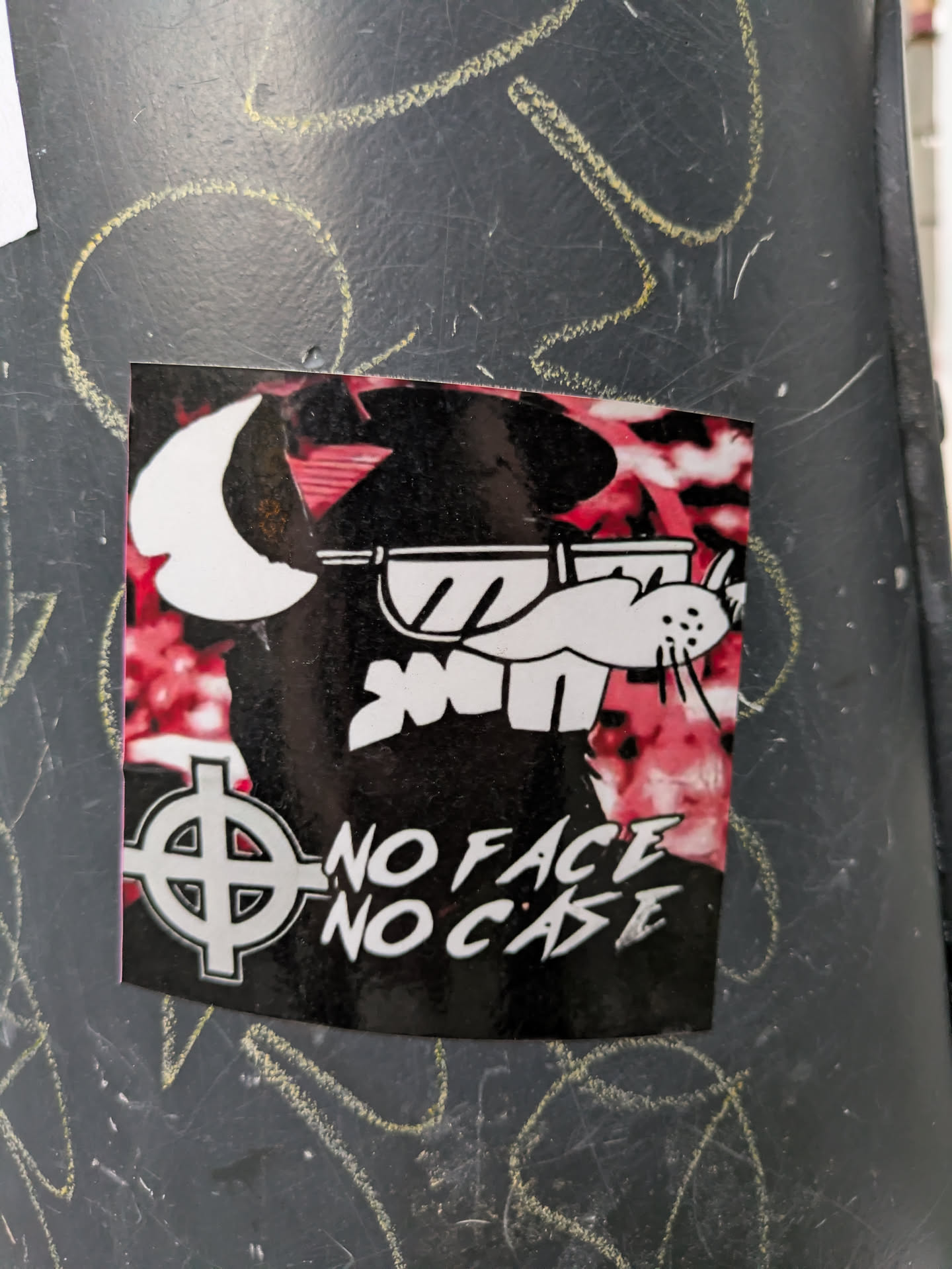 The sticker features a stylized illustration of a white cartoonish character wearing sunglasses, set against a red and black background. The text "NO FACE NO CASE" is prominently displayed below the illustration, accompanied by a symbol resembling a circle with a cross inside.